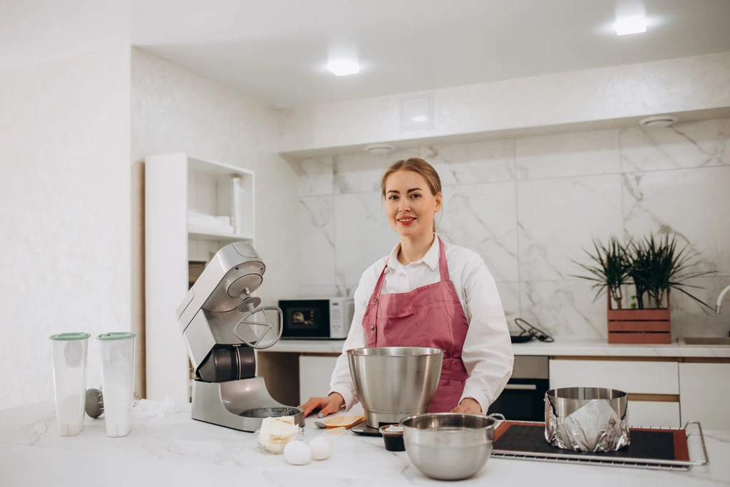 A portrait of Emily Harrison, the creator of Cookery Command, standing at her kitchen counter with baking ingredients.