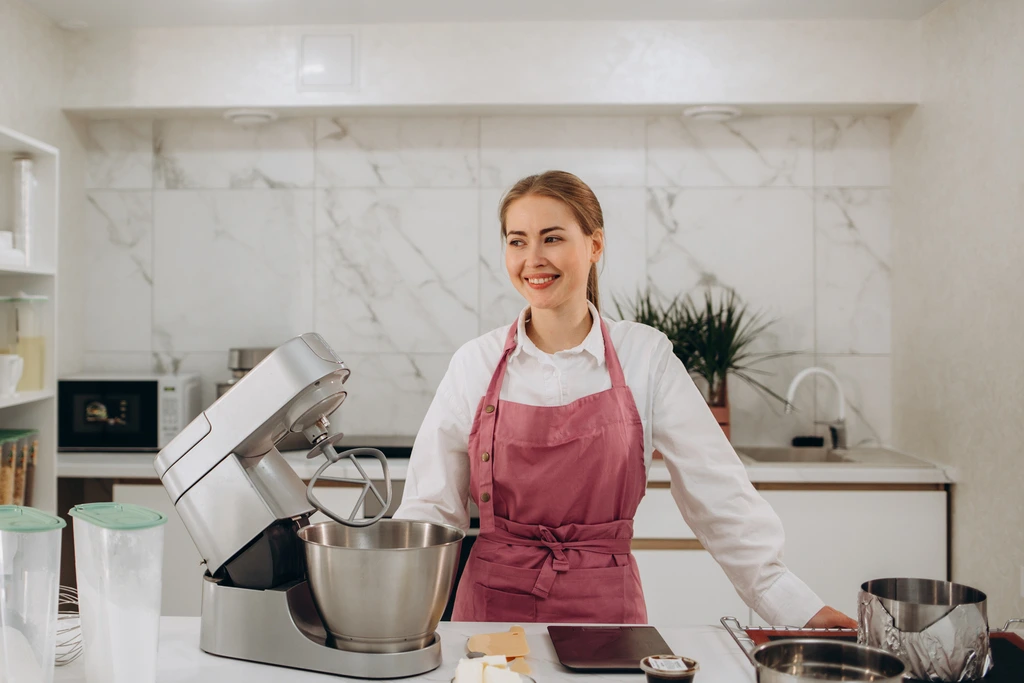 Emily Harrison, author of Cookery Command, smiling in her kitchen while standing next to a stand mixer