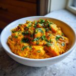 A close-up of vibrant orange pumpkin curry served in a white bowl and garnished with fresh chopped cilantro.