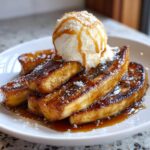 Close-up of caramelized bananas foster topped with vanilla ice cream, caramel drizzle, and coconut flakes.