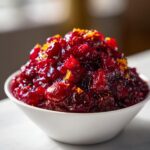 A close-up of vibrant, chunky homemade cranberry sauce topped with bright orange zest, served in a white bowl.