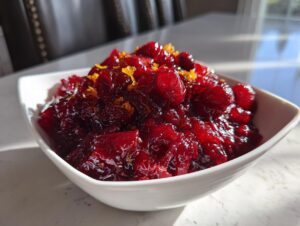 Close-up of vibrant, homemade cranberry sauce topped with bright orange zest in a white bowl.