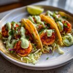 Three delicious shrimp taco shells filled with seasoned shrimp, cabbage slaw, and drizzled generously with a creamy green sauce.