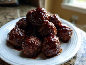 A pile of glistening, saucy grape jelly meatballs served on a white plate.