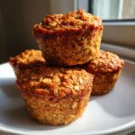 A stack of three golden brown banana oatmeal muffins with visible oats on a white plate.