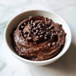 A close-up of thick, rich brownie batter dip topped generously with mini chocolate chips in a white bowl.