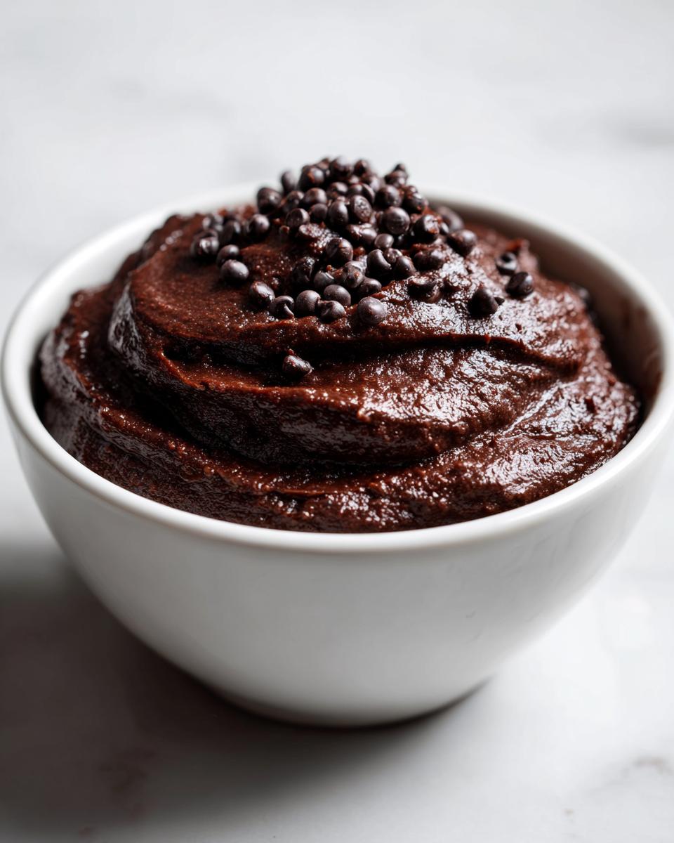 A close-up of rich, dark brownie batter dip served in a white bowl and topped with mini chocolate chips.