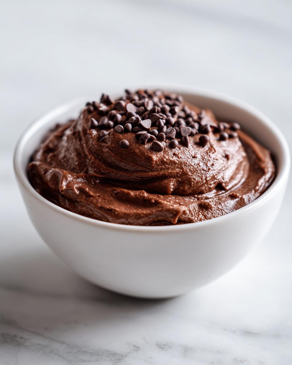 A close-up of rich, thick brownie batter dip served in a white bowl, topped generously with mini chocolate chips.