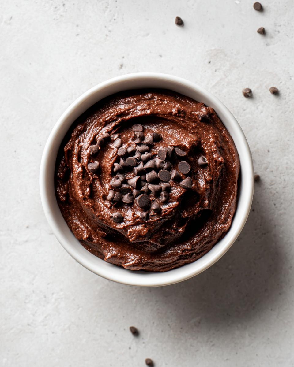 Overhead view of rich, dark chocolate brownie batter dip in a white bowl, topped with mini chocolate chips.