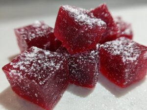 A close-up stack of vibrant red, square Candy Cane Fireball Gummies dusted with white powdered sugar.