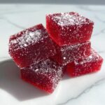 A small stack of deep red, square Candy Cane Fireball Gummies dusted with sugar crystals.