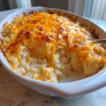 A close-up of a baked cheesy chicken and rice casserole topped with bubbly, browned cheddar cheese.