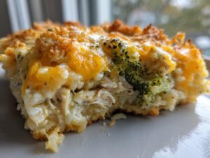 A close-up, mouth-watering slice of chicken broccoli rice casserole featuring shredded chicken, rice, and melted cheddar cheese topping.