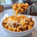 A spoonful of homemade hamburger helper being lifted from a bowl, showing melted, stretching cheese and ground beef.