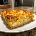 A square slice of baked cheesy potato casserole with a deeply browned, golden cheese topping.