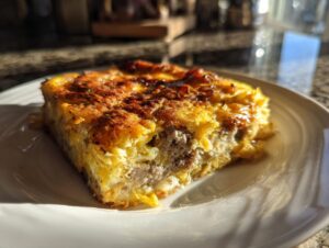 A close-up, sunlit slice of savory Christmas breakfast casserole featuring eggs and sausage on a white plate.
