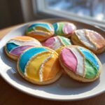 A plate of sugar cookies decorated with vibrant, multi-colored royal sugar cookie icing designs.