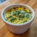 Close-up of melted cowboy butter dipping sauce, rich yellow with fresh green chives on top, served in a white ramekin.