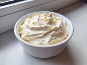 A close-up of thick, creamy garlic aioli swirled in a small white bowl, lightly seasoned.