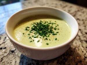 A close-up of a bowl of creamy, light green leek soup garnished with fresh chopped chives and pepper.