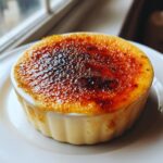 Close-up of a single serving of Creme brulee with a dark, glassy, torched sugar crust.