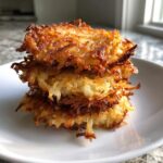 A tall stack of three golden brown, crispy Potato latkes served on a white plate.
