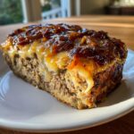 A close-up slice of crockpot french onion meatloaf topped with melted cheese and caramelized onions.