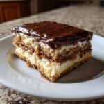 A perfect square slice of eclair cake showing layers of graham crackers, vanilla cream, and chocolate frosting.