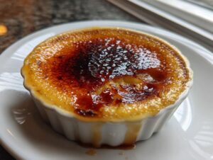 Close-up of a freshly made creme brulee with a dark, crackled caramelized sugar top, served in a white ramekin.