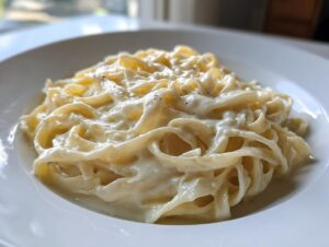 Close-up of fettuccine pasta generously coated in creamy homemade alfredo sauce, sprinkled with pepper.