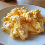 Close-up of perfectly cooked, fluffy scrambled eggs piled high on a white plate.