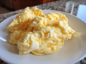 Close-up of soft, creamy scrambled eggs piled high on a white plate, ready to eat.