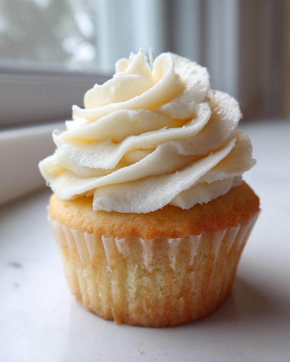 A single, beautifully frosted vanilla cupcake with white buttercream swirls, ready to eat.