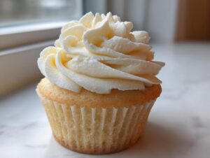 A single, perfectly baked vanilla cupcake topped with a generous swirl of creamy white vanilla frosting.