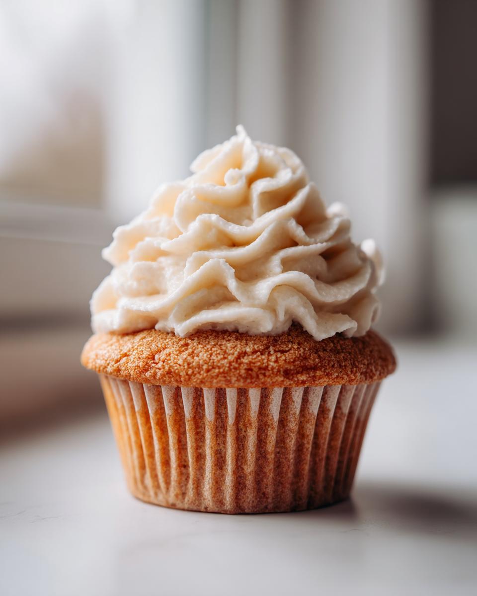 A single, fluffy vanilla cupcakes with a generous swirl of creamy vanilla frosting, set against a bright background.