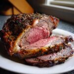 Close-up of a perfectly cooked rib roast, sliced to show the medium-rare pink center and herb crust.