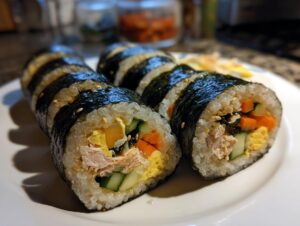 Close-up of several slices of homemade tuna kimbap featuring rice, seaweed, tuna, egg, and vegetables.