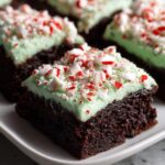 Close-up of a fudgy peppermint brownies square topped with light green mint frosting and crushed candy canes.