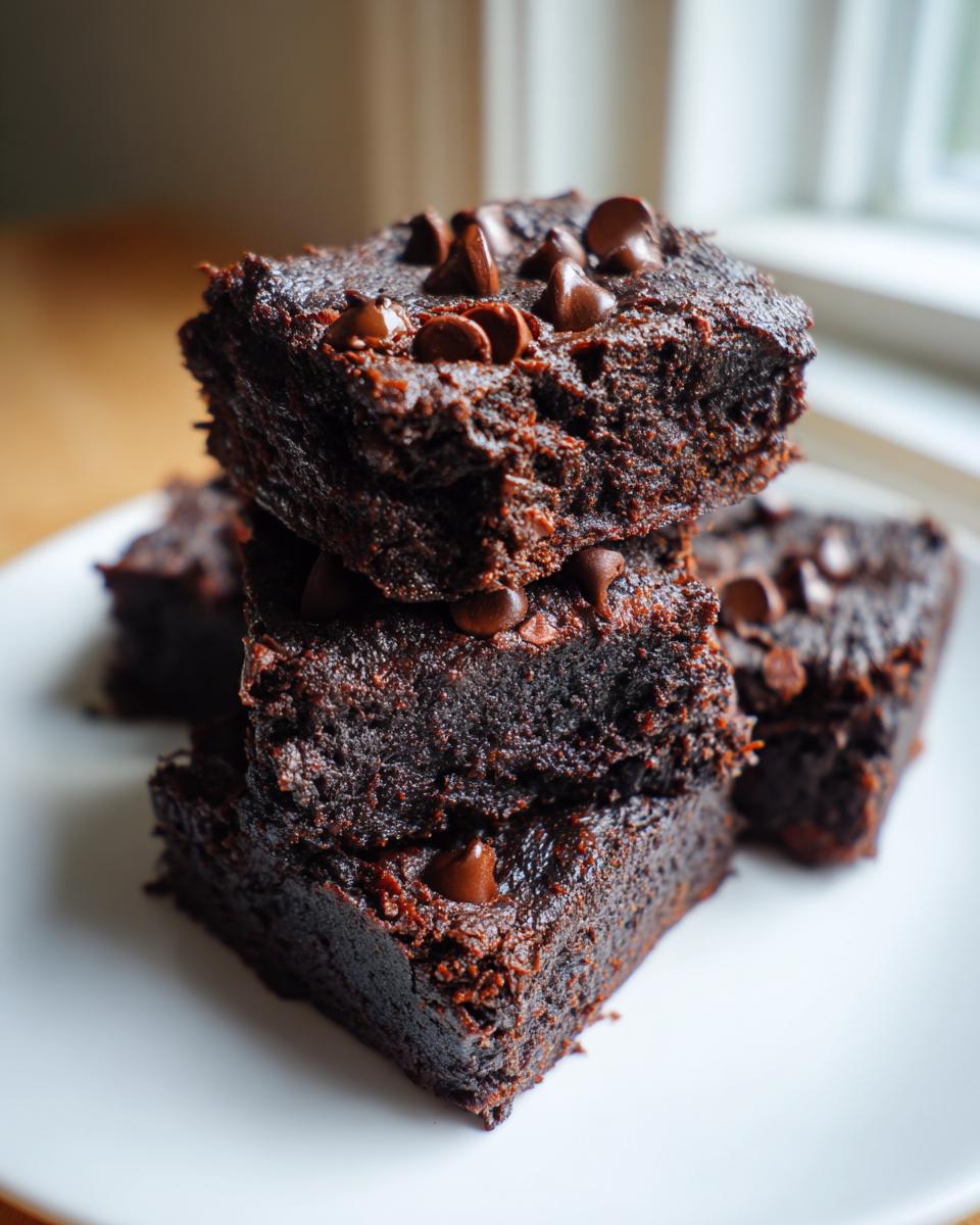 A stack of three rich, dark, fudgy sweet potato brownies topped with melted chocolate chips on a white plate.