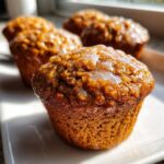 A close-up, sunlit photo of three rich brown honey bran muffins topped with a shiny, thin glaze.
