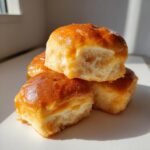 A stack of three fluffy, golden-brown sweet potato rolls with a shiny glaze, showing the soft interior texture.