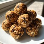 A stack of homemade chocolate chip protein balls made with visible oats, sitting on a white plate.