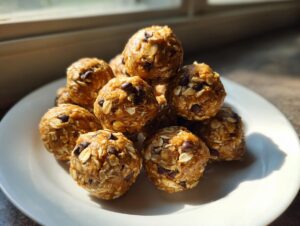 A stack of homemade chocolate chip protein balls made with oats, sitting on a white plate near a window.
