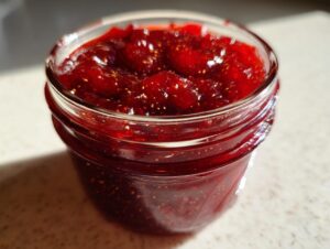 Close-up of a jar filled with glistening, deep red homemade christmas jam, showing visible seeds.