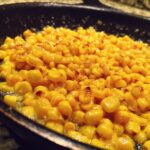 Close-up of bright yellow corn kernels sizzling in butter in a dark cast iron skillet, perfect for a honey butter corn side.
