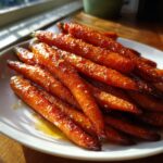 A pile of perfectly cooked, shiny honey glazed carrots glistening with glaze on a white serving dish.