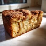 Close-up of a moist slice of jewish apple cake showing chunks of apple and a cinnamon-sugar topping.