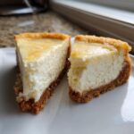 Two delicious slices of creamy Keto cheesecake with a thick graham cracker crust resting on a white plate.