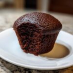 Close-up of a rich, dark brown, unfrosted easy chocolate cupcakes with a bite taken out, sitting on a white plate.