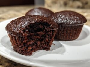 Close-up of moist, dark chocolate cupcakes, one with a bite taken out, showing the rich crumb texture of the easy chocolate cupcakes.